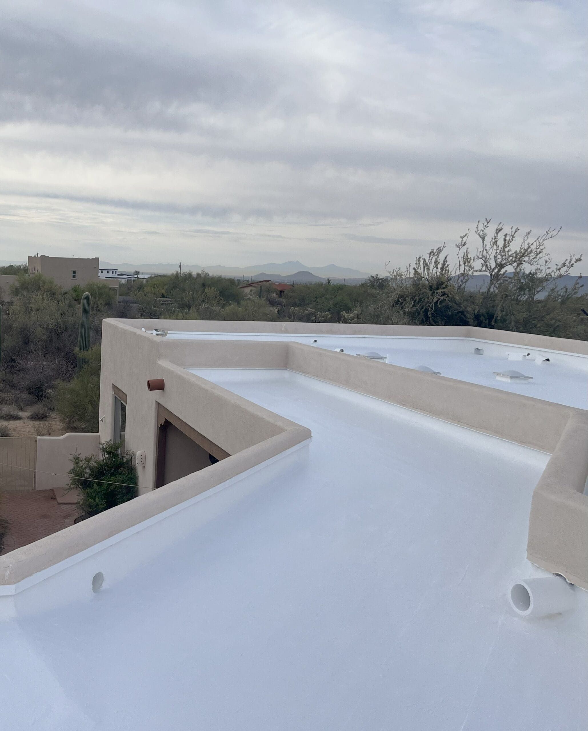 Flat rooftop with fresh white coating, showcasing recent repair by a roofing maintenance company against a desert landscape backdrop.