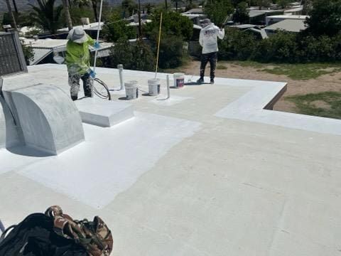 Roofing professionals applying white coating on a flat roof, showcasing maintenance and repair work by a roofing company.