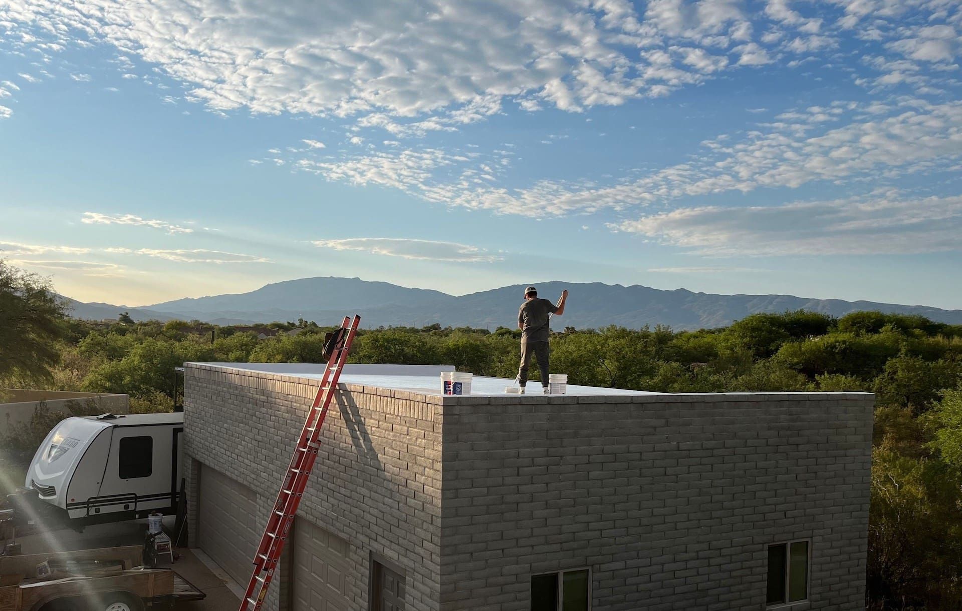 Workers applying a white coating to a flat roof with parapet walls, showing a maintenance process.