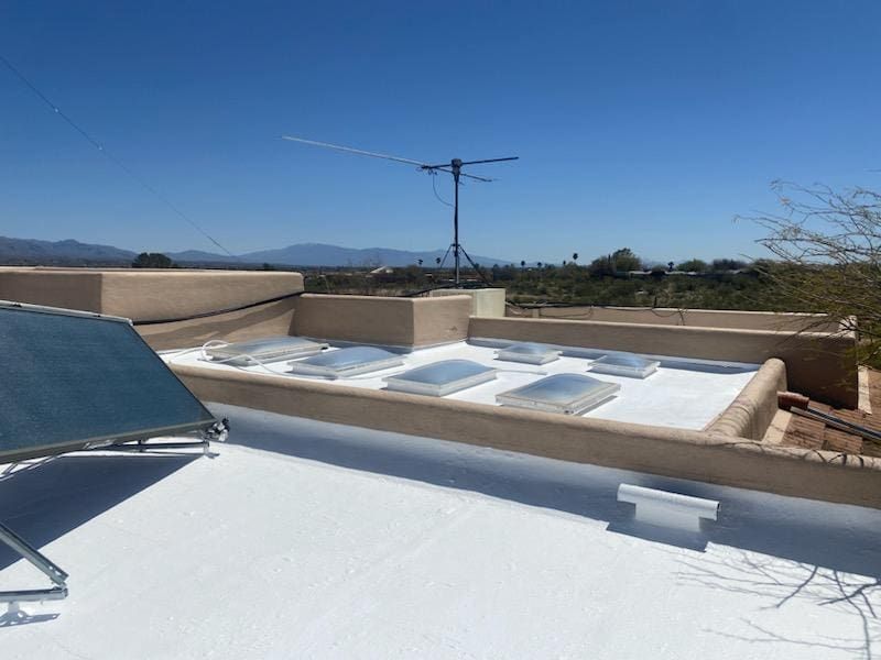 Flat white roof with multiple skylights and a solar panel, showing a well-maintained roofing surface on a clear sunny day.