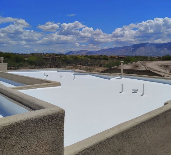 Workers applying a white coating to a flat roof with parapet walls, showing a maintenance process.