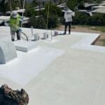 Roofing professionals applying white coating on a flat roof, showcasing maintenance and repair work by a roofing company.